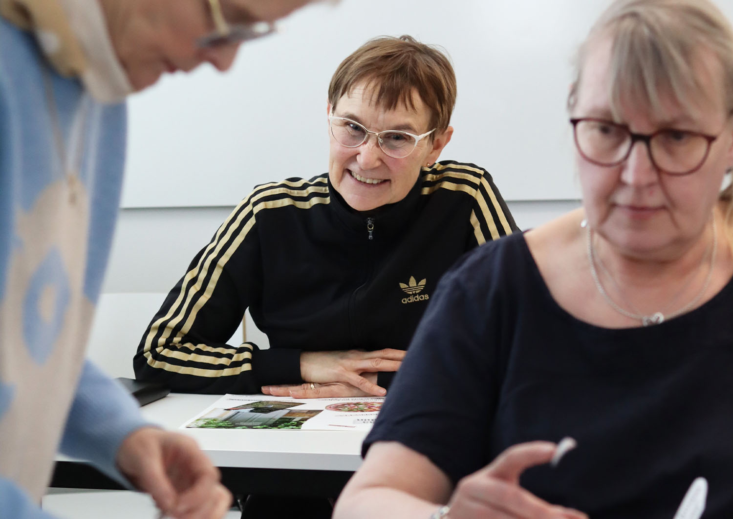 Kuvassa iloinen nainen kurkistaa kahden muun naisen takaa
