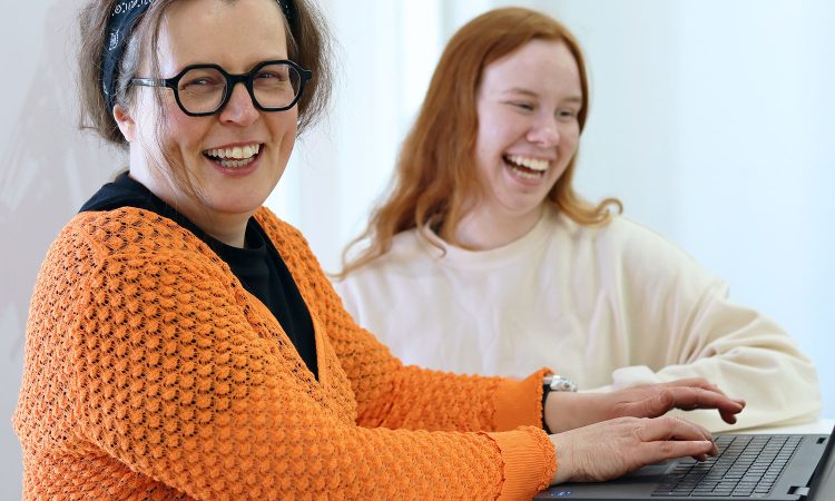 Kaksi iloista naista kannettavan tietokoneen ääressä