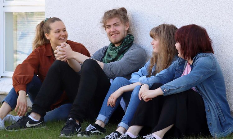 Kuva neljästä opiskelijasta istumassa nurmikolla hymyillen.