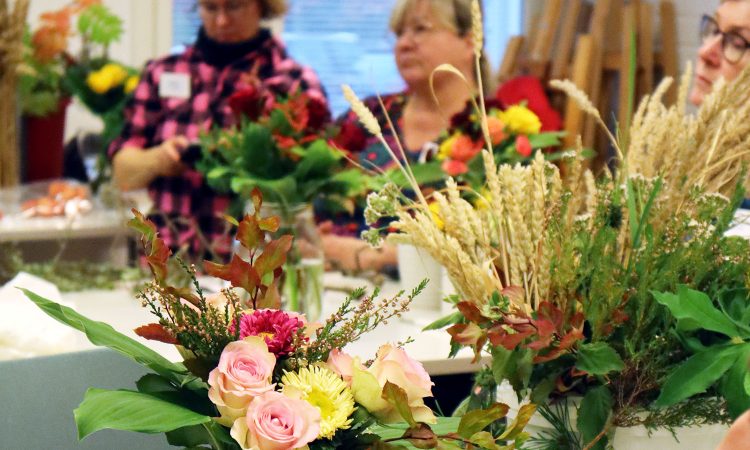 etualalla erilaisia kukkakimppuja, takana naisia sitomassa kimppuja
