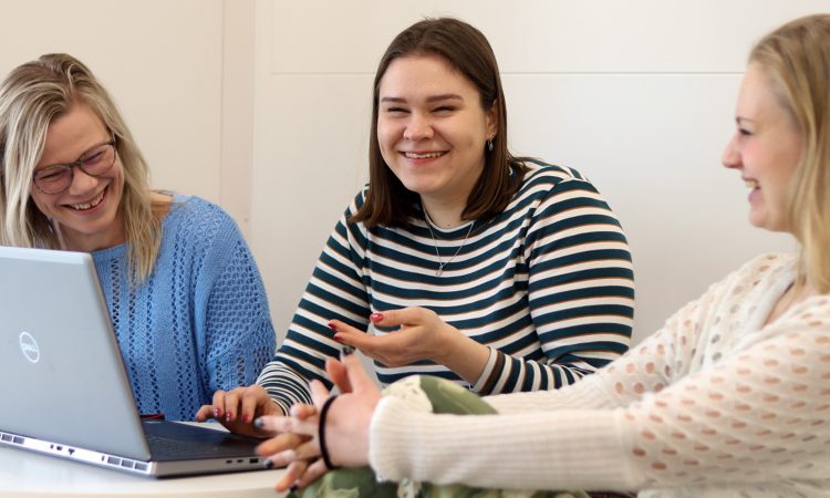 Kolme iloista henkilöä kannettavan tietokoneen äärellä